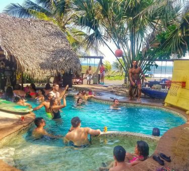 Fun travelers having fun in the pool and drinking beer at the Driftwood Surfer in El Paredon, Guatemala
